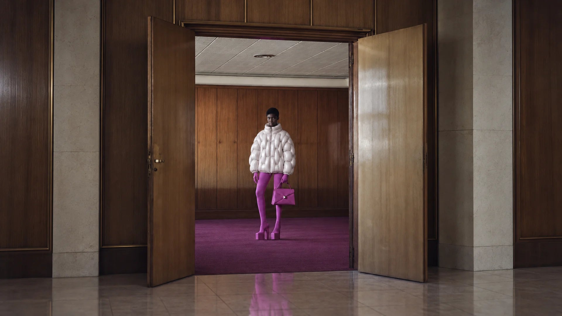 Model in a walnut doorway wearing the white OCTAGON Pentagon high-gloss puffer jacket