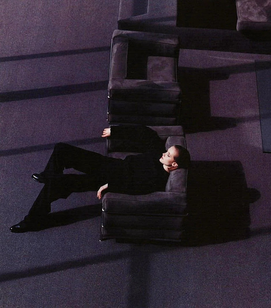 Model reclining among geometric lounge seating in a deep plum interior